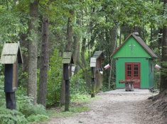 Drewaniana, zielona kapliczka i 3 stacje drogi krzyżowej na ścieżce w lesie.